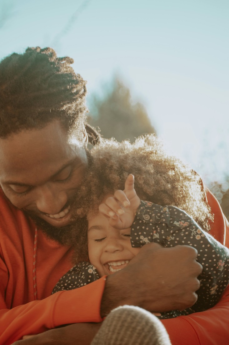 A father hugging his laughing daughter outside